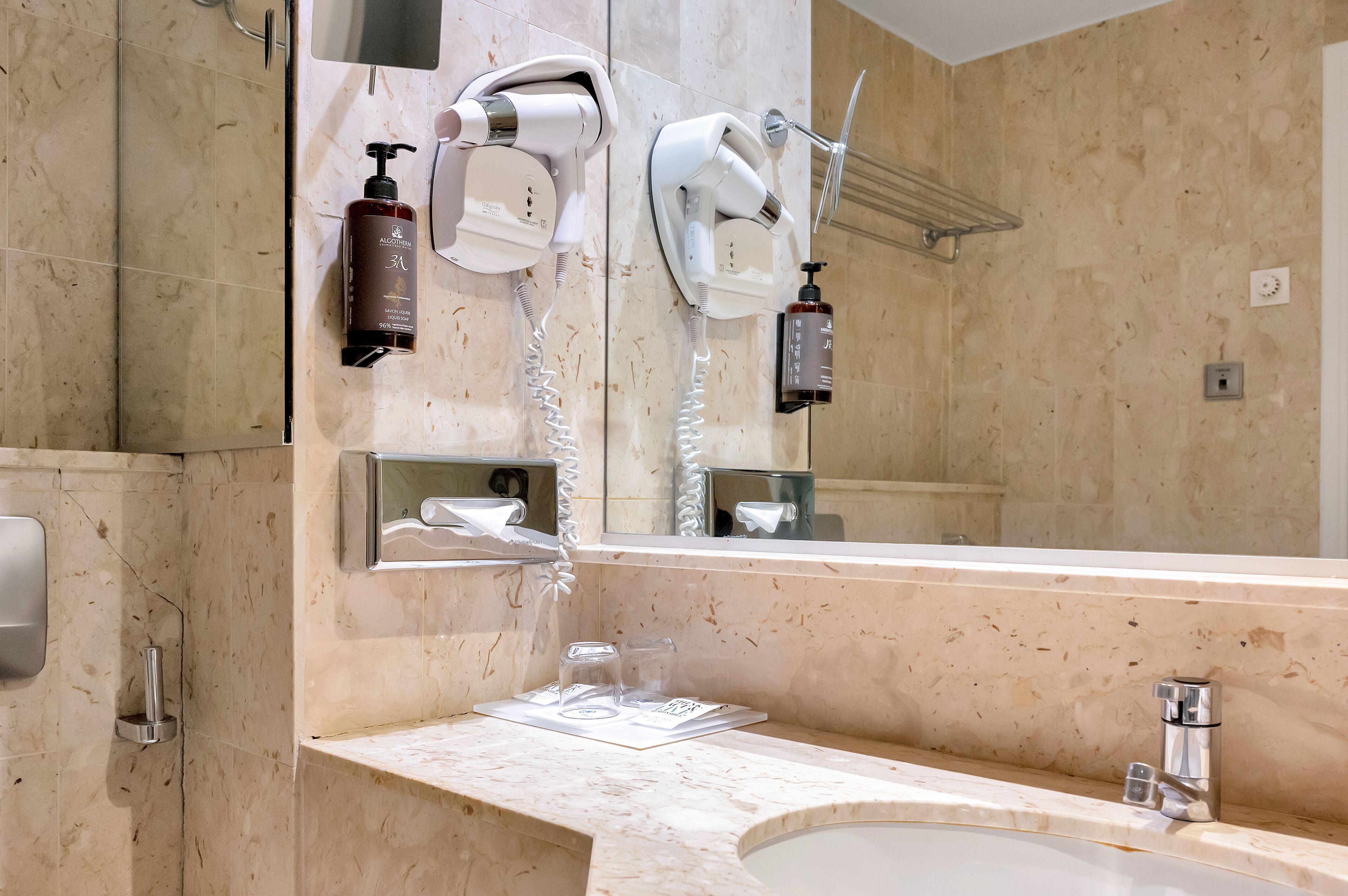 A bathroom with a marble sink, a mirror, a hairdryer, and a towel rack.