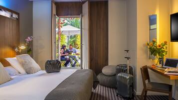 A hotel room with a bed, a desk with a laptop, a chair, and two suitcases.