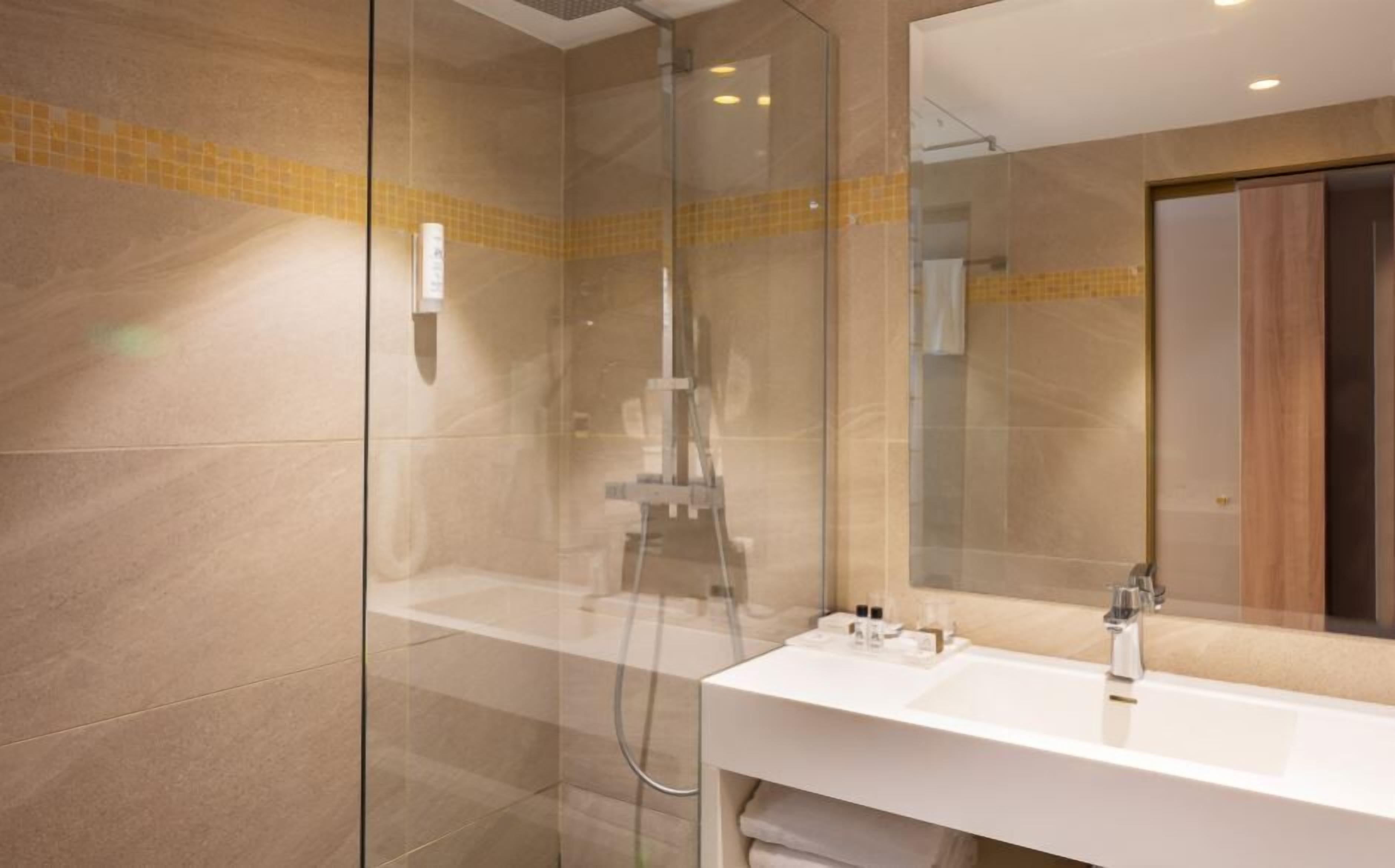 A modern bathroom with a glass-enclosed shower, a white sink, and a mirror reflecting the room.