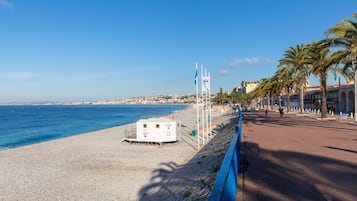 Un passeig marítim amb una platja de pedres, una posta de socors i una filera de palmeres.