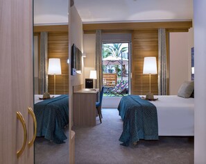 A hotel room with two beds, a desk, a chair, and a view of an outdoor area with a pool and umbrellas.