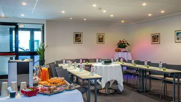 A conference room with tables set for a meeting, equipped with water bottles, apples, and a coffee station.