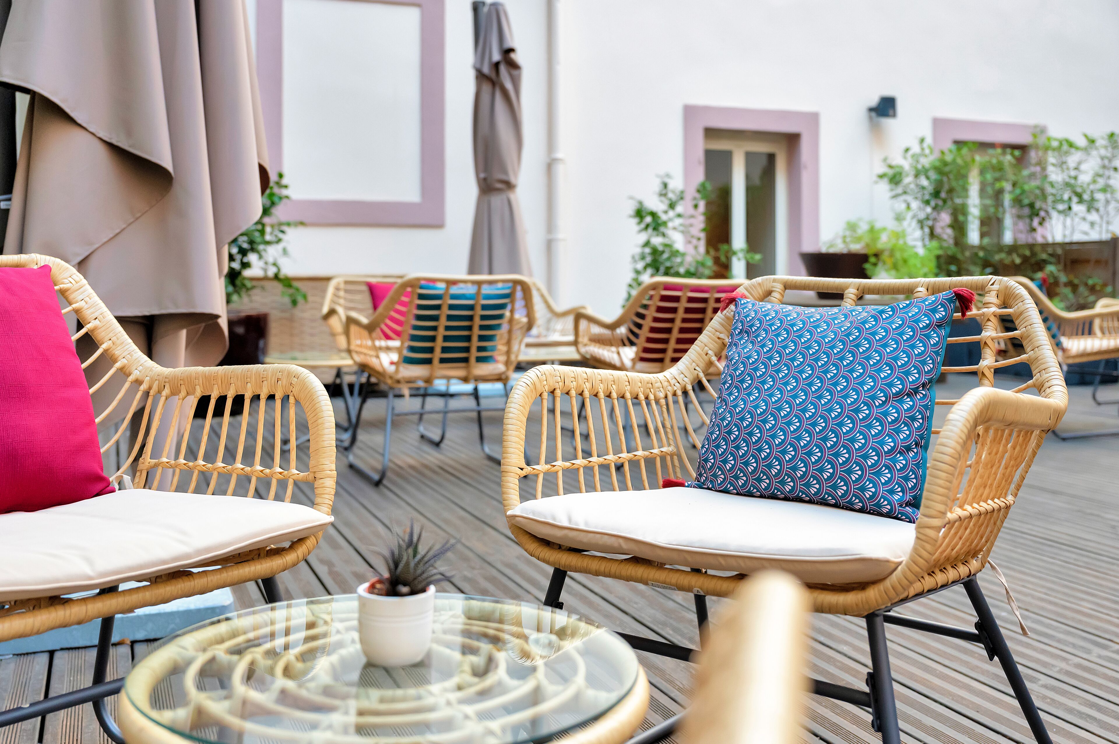 Wicker chairs with cushions and a glass table with a potted plant.