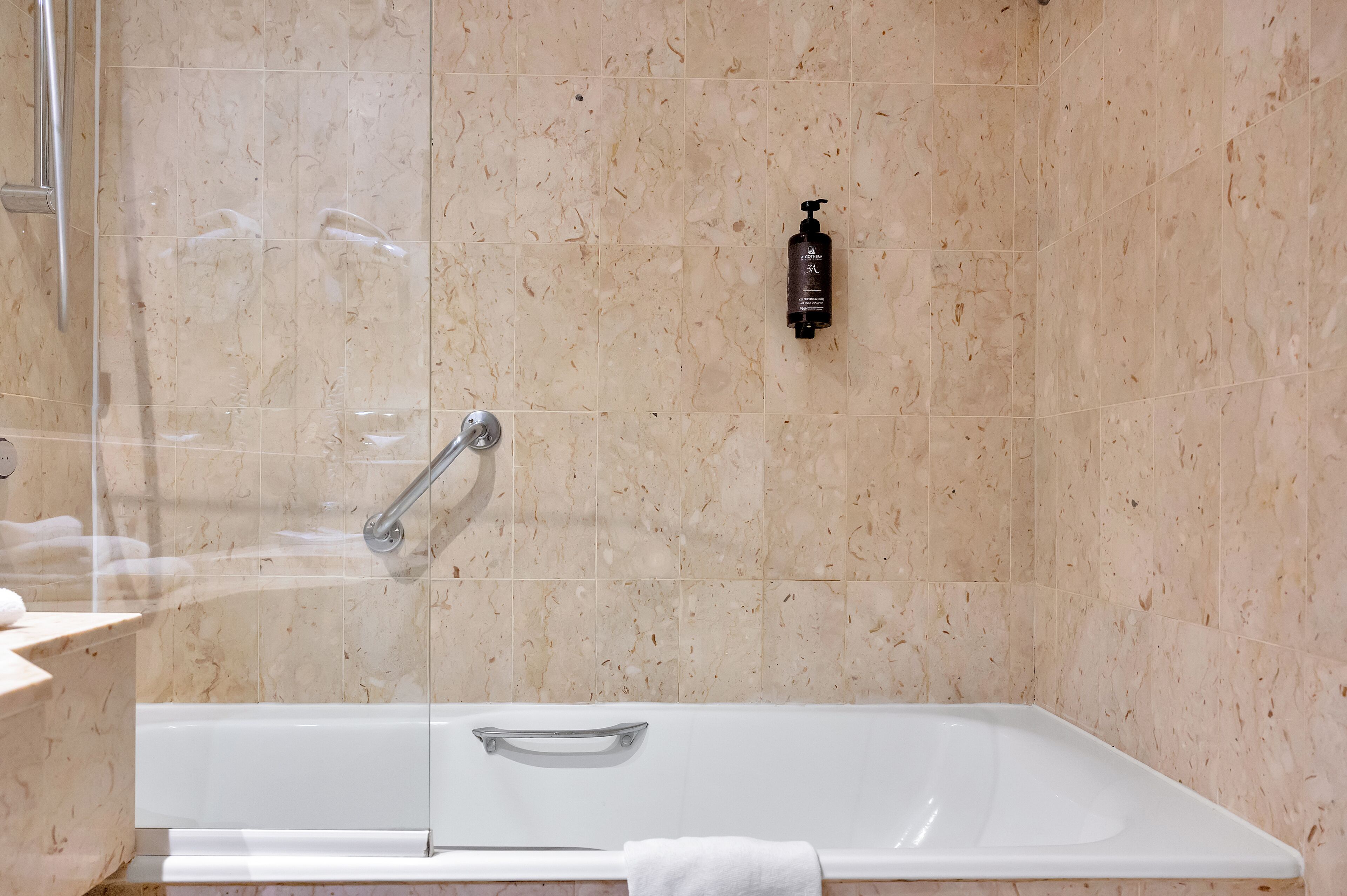 Un baño moderno con ducha envuelta en vidrio, una bañera blanca y un revestimiento de mármol.
