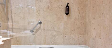 Un baño moderno con ducha envuelta en vidrio, una bañera blanca y un revestimiento de mármol.