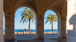 Una estructura arquitectónica con arcos y palmeras que conduce a una playa.