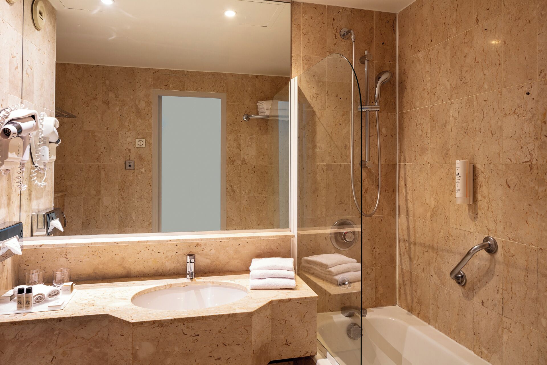 Un baño moderno con lavamanos de mármol, ducha con mampara de vidrio y un espejo grande.