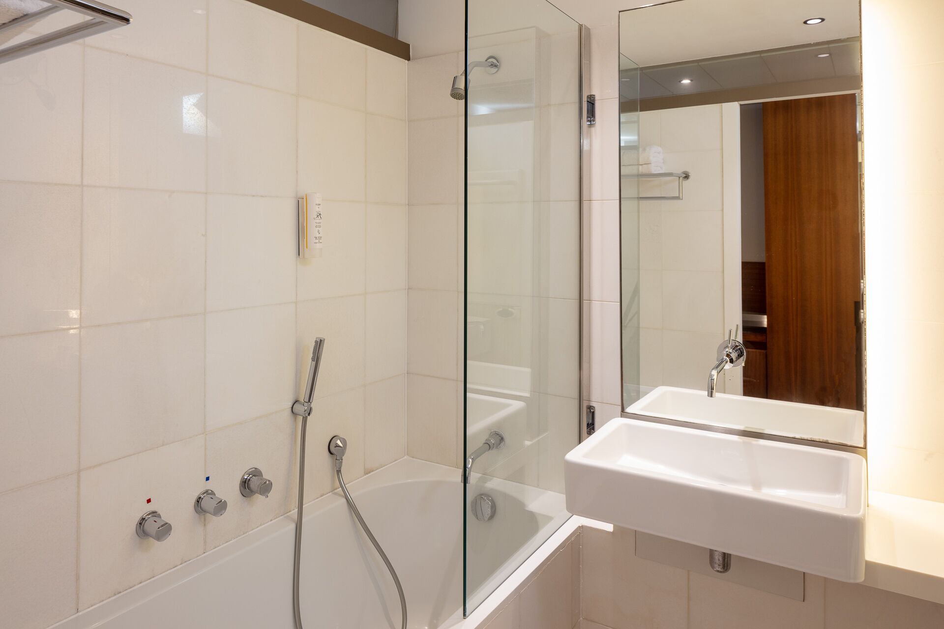 A modern bathroom with a glass-enclosed shower, a bathtub, and a sink with a mirror above it.