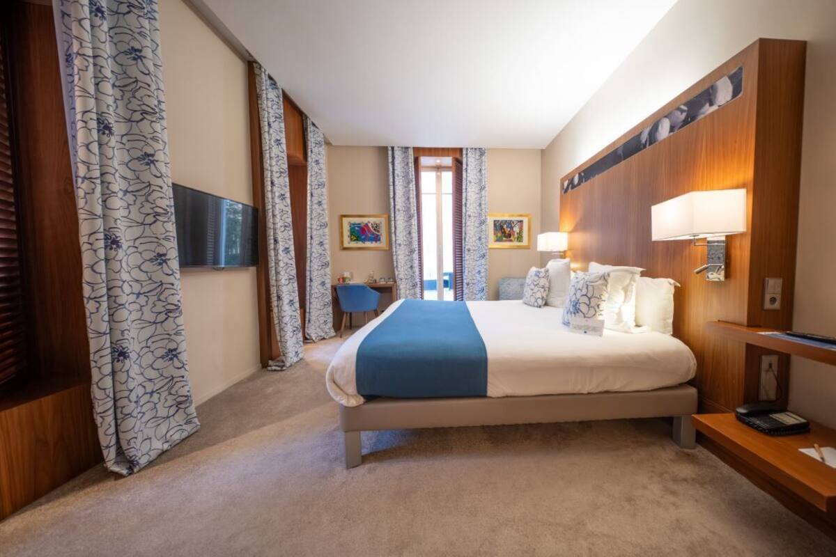 A hotel room with a bed, a desk, a chair, a TV, and a window.