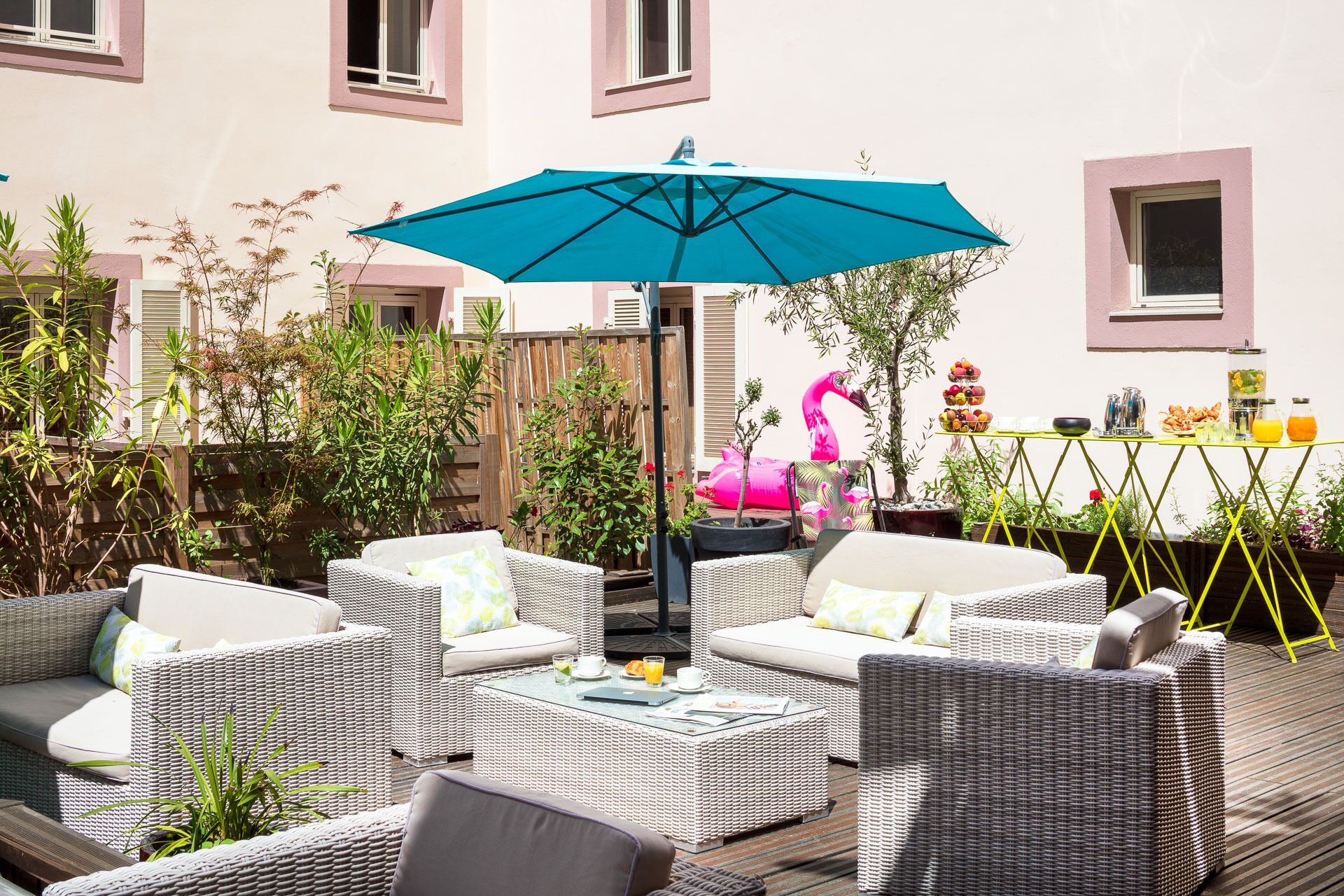 Un patio al aire libre con mobiliario de mimbre, un paraguas azul y una mesa con comida y bebidas.