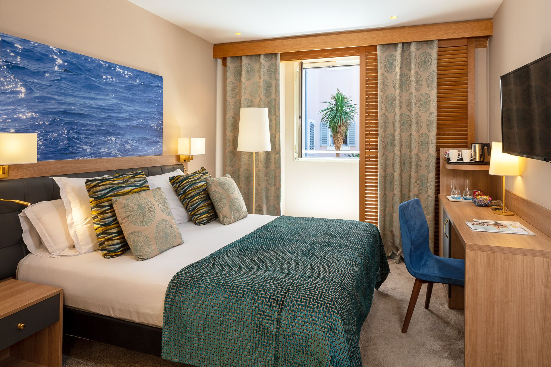 Habitación de hotel con cama, escritorio, silla, televisor y ventana con cortinas.