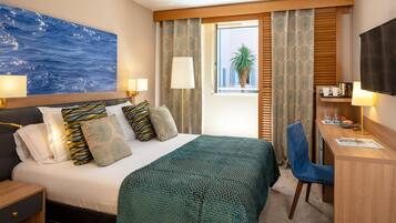 Habitación de hotel con cama, escritorio, silla, televisor y ventana con cortinas.