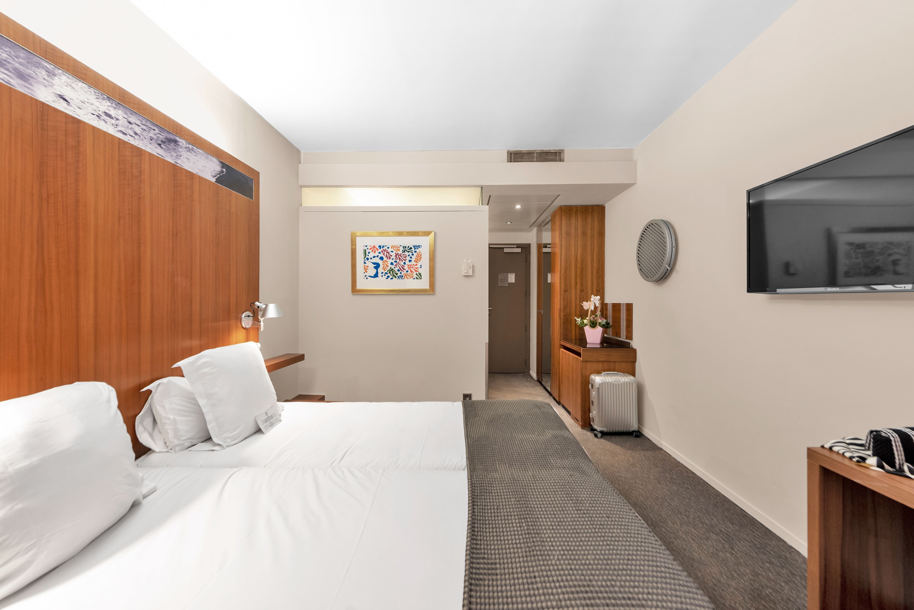 Een hotelkamer met een bed, een bureau, een televisie en een badkamer op de achtergrond.