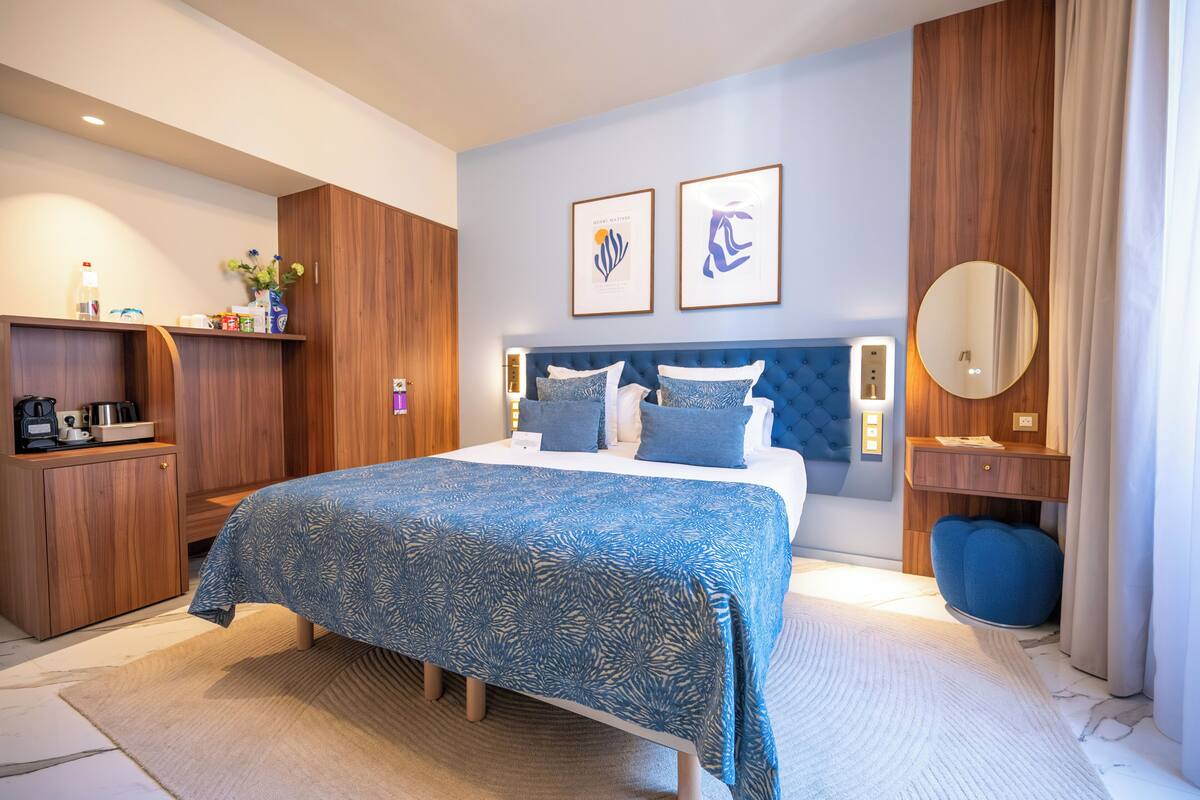 A hotel room with a bed, wooden wardrobe, bedside table, and a mirror.