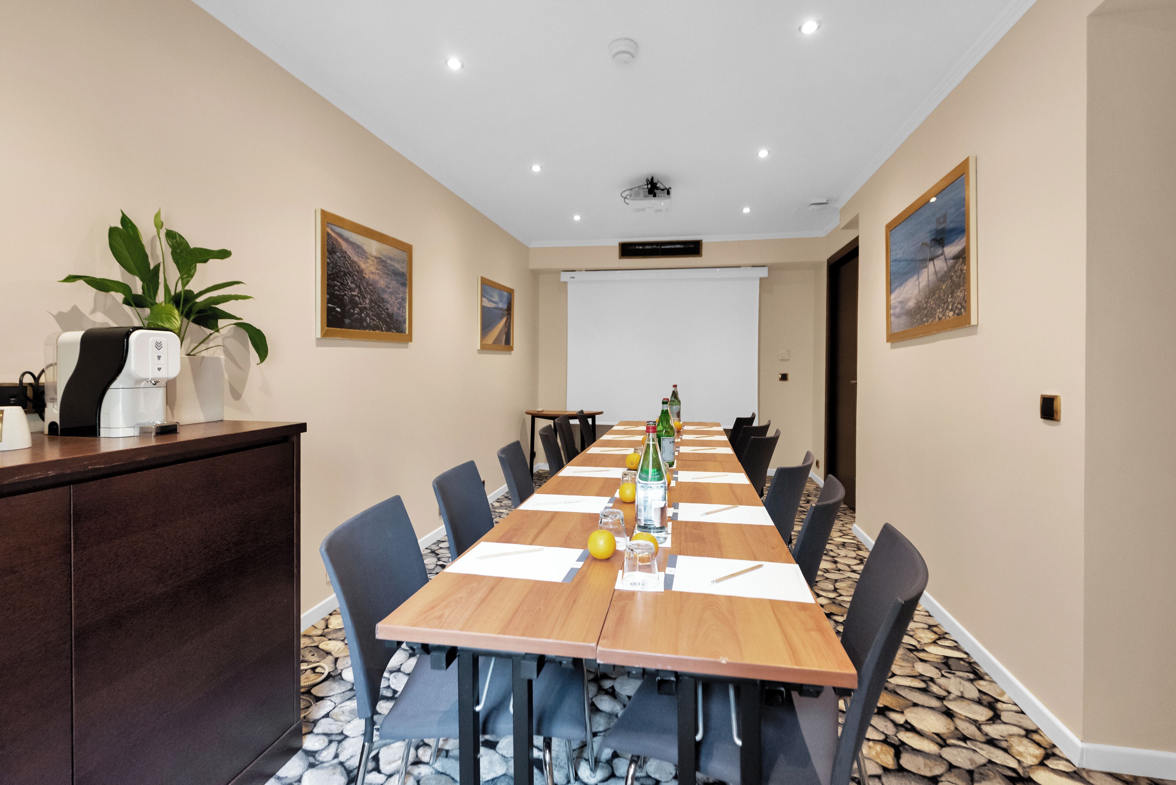 Un salón de conferencias con una larga mesa, sillas, una pantalla de proyector y una máquina de café.