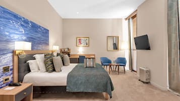 A hotel room with a bed, bedside lamps, a desk, a chair, a television, and a large painting on the wall.