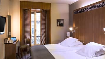 Une chambre d’hôtel avec un lit, un bureau avec un ordinateur, une chaise et une fenêtre avec des stores.