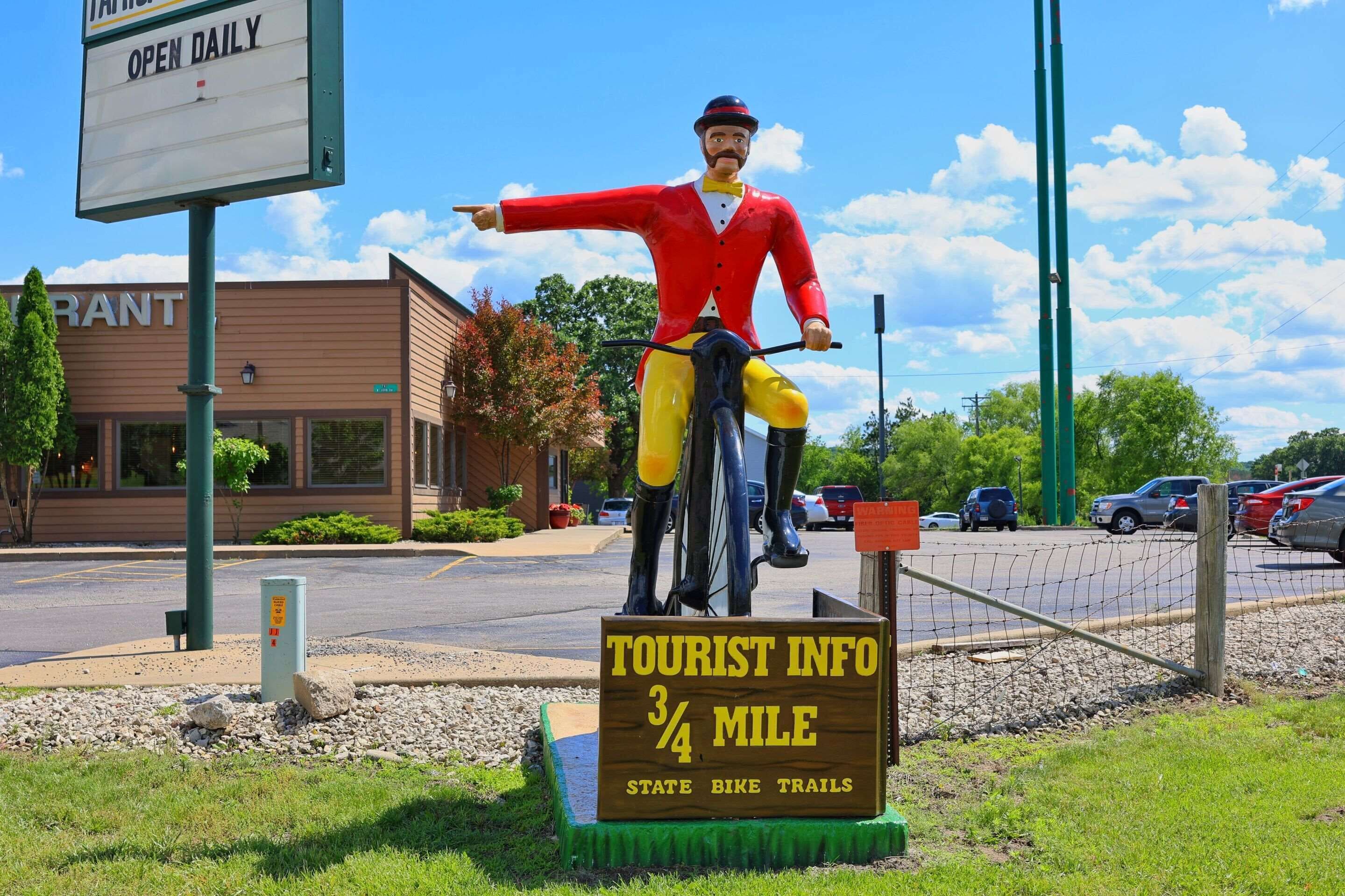 Un panneau d’information touristique avec une statue de cycliste, un bâtiment portant l’inscription « GRANT » et un parking.