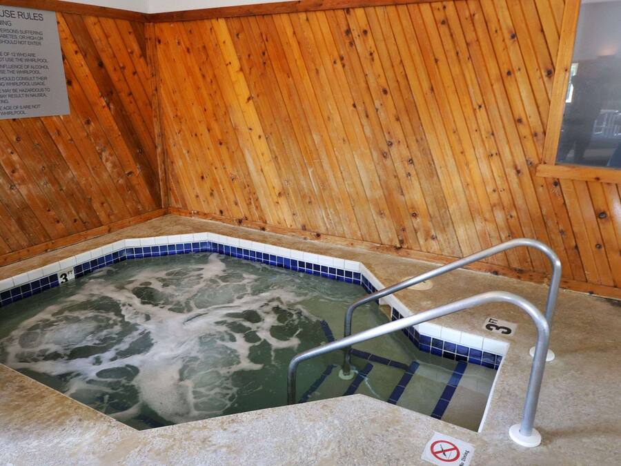 A wooden-floored whirlpool with a blue-tiled edge, a metal handrail, and a warning sign about whirlpool use rules.