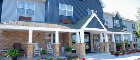 A Country Inn & Suites by Radisson with a covered front porch, outdoor seating, and a variety of potted plants and flowers.