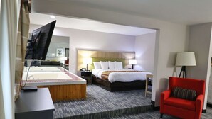 Une chambre d’hôtel avec un lit, un fauteuil rouge, un bureau avec un ordinateur et une télévision.
