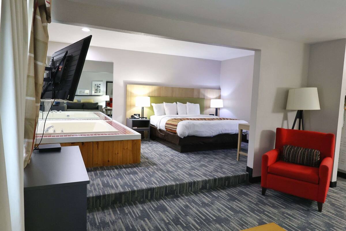 A hotel room with a bed, a red armchair, a desk with a computer, and a TV.