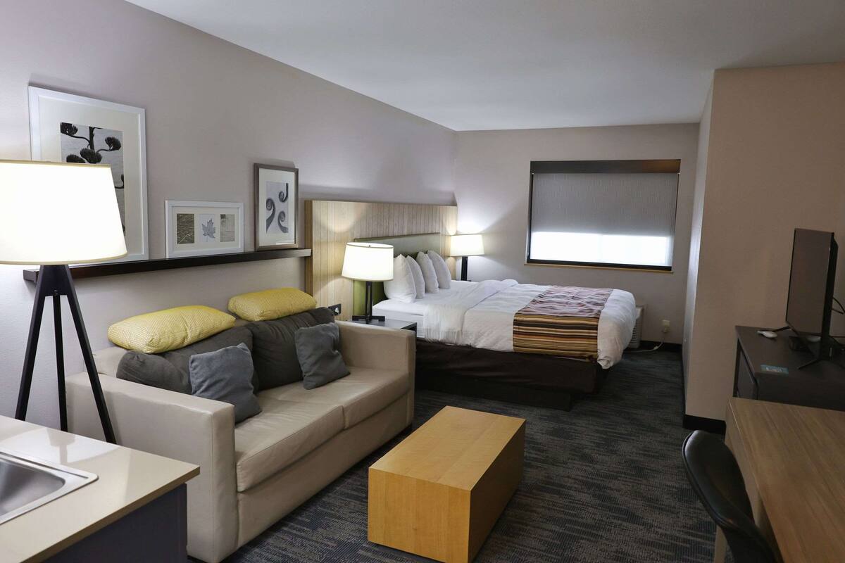 A hotel room with a bed, a sofa, a desk, a lamp, and framed pictures on the wall.