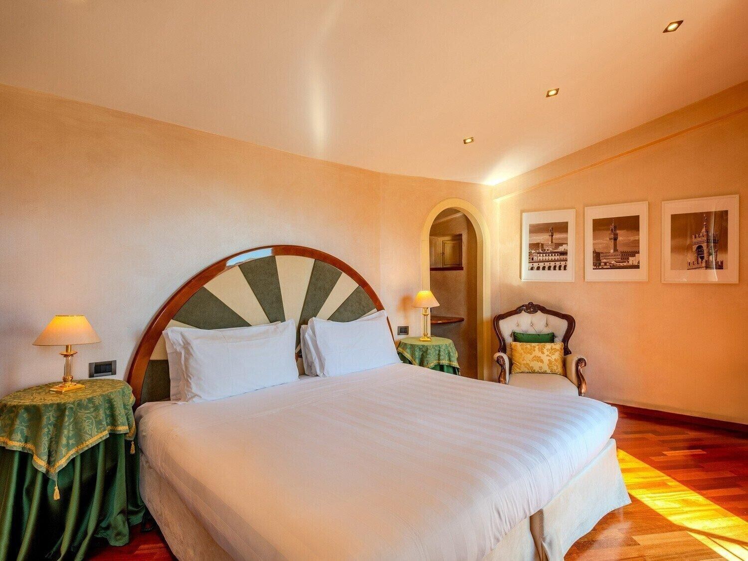 Ein Hotelzimmer mit einem großen Bett, zwei Nachttischen inklusive Lampen, einem Holzstuhl und drei gerahmten Bildern an der Wand.