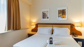 Une chambre d’hôtel avec un lit double, deux tables de chevet, une commode, un téléphone, une lampe et deux tableaux encadrés au mur.