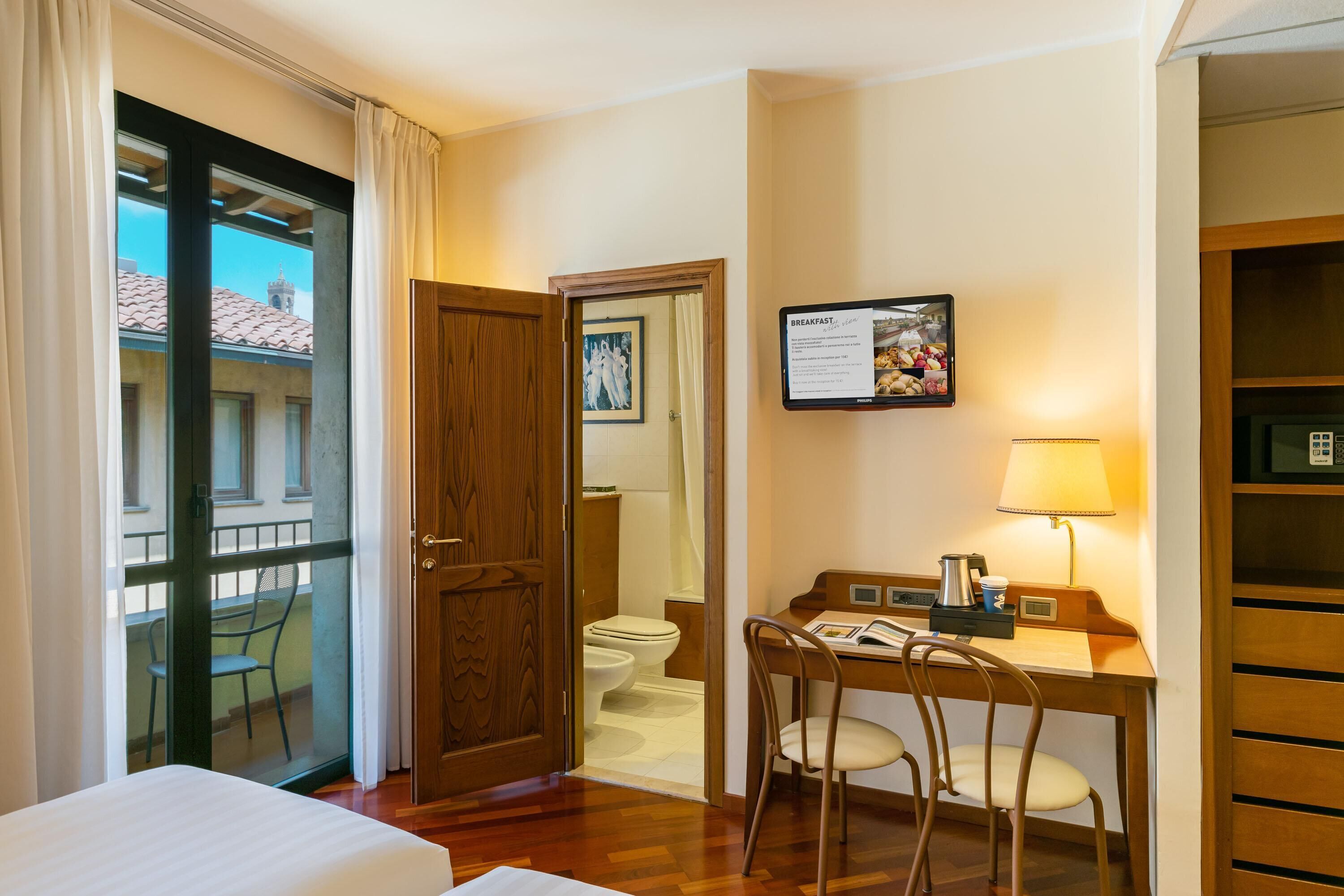 Een hotelkamer met een bed, een bureau met stoel, een badkamer en uitzicht.