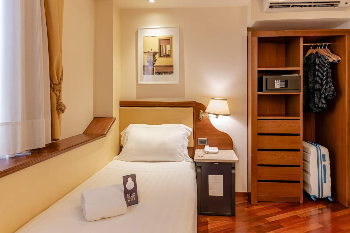 A hotel room with a bed, bedside table, lamp, wardrobe, and a suitcase.