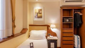 Ein Hotelzimmer mit Bett, Nachttisch, Lampe, Kleiderschrank und Koffer.