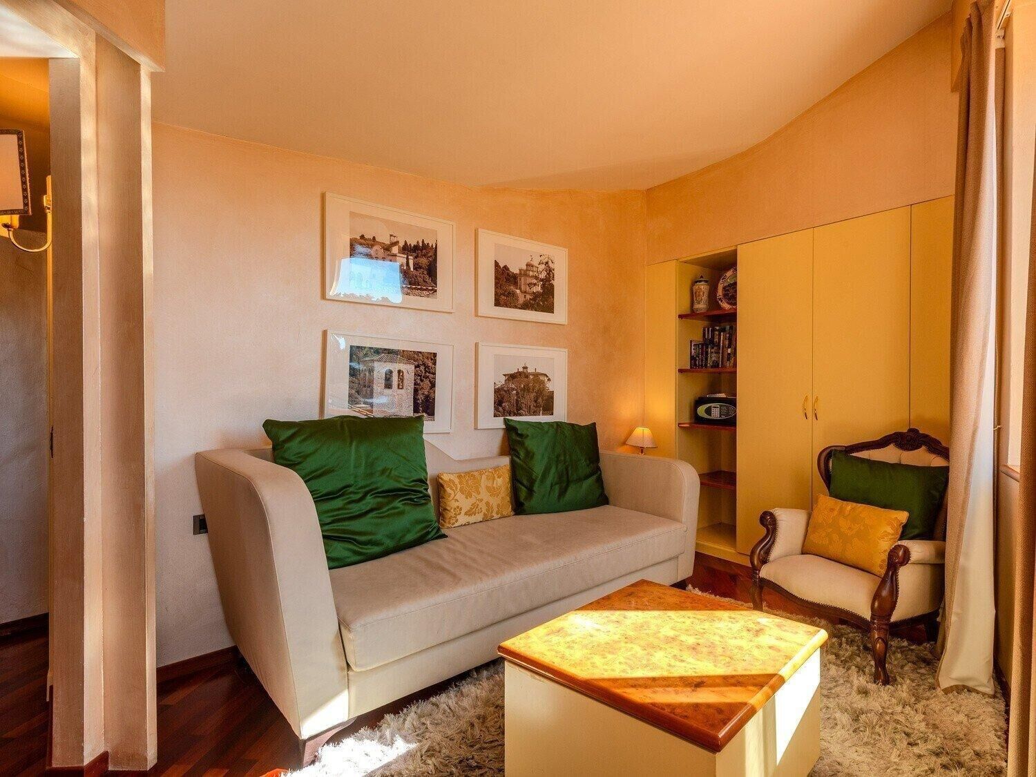 A living room with a beige sofa, green and yellow cushions, a wooden coffee table, and a bookshelf with books and decorative items.