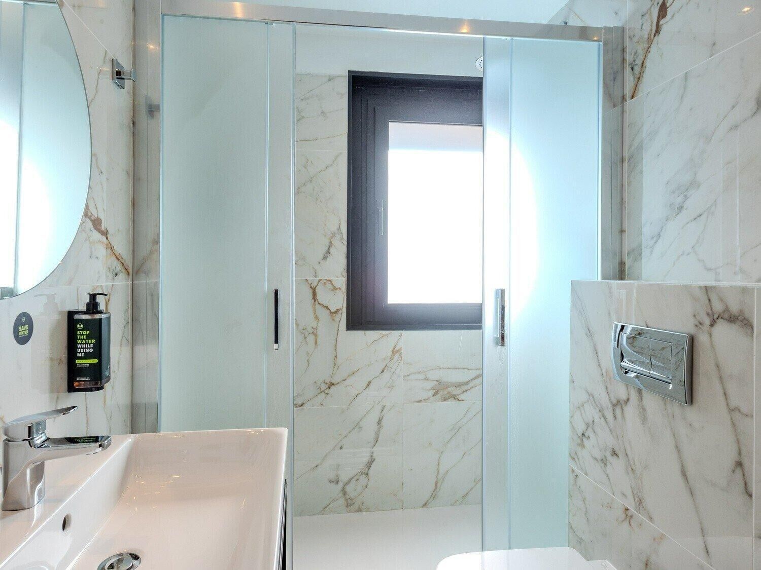 Une salle de bain moderne avec une douche à l’italienne en verre, un grand miroir et un lavabo blanc.