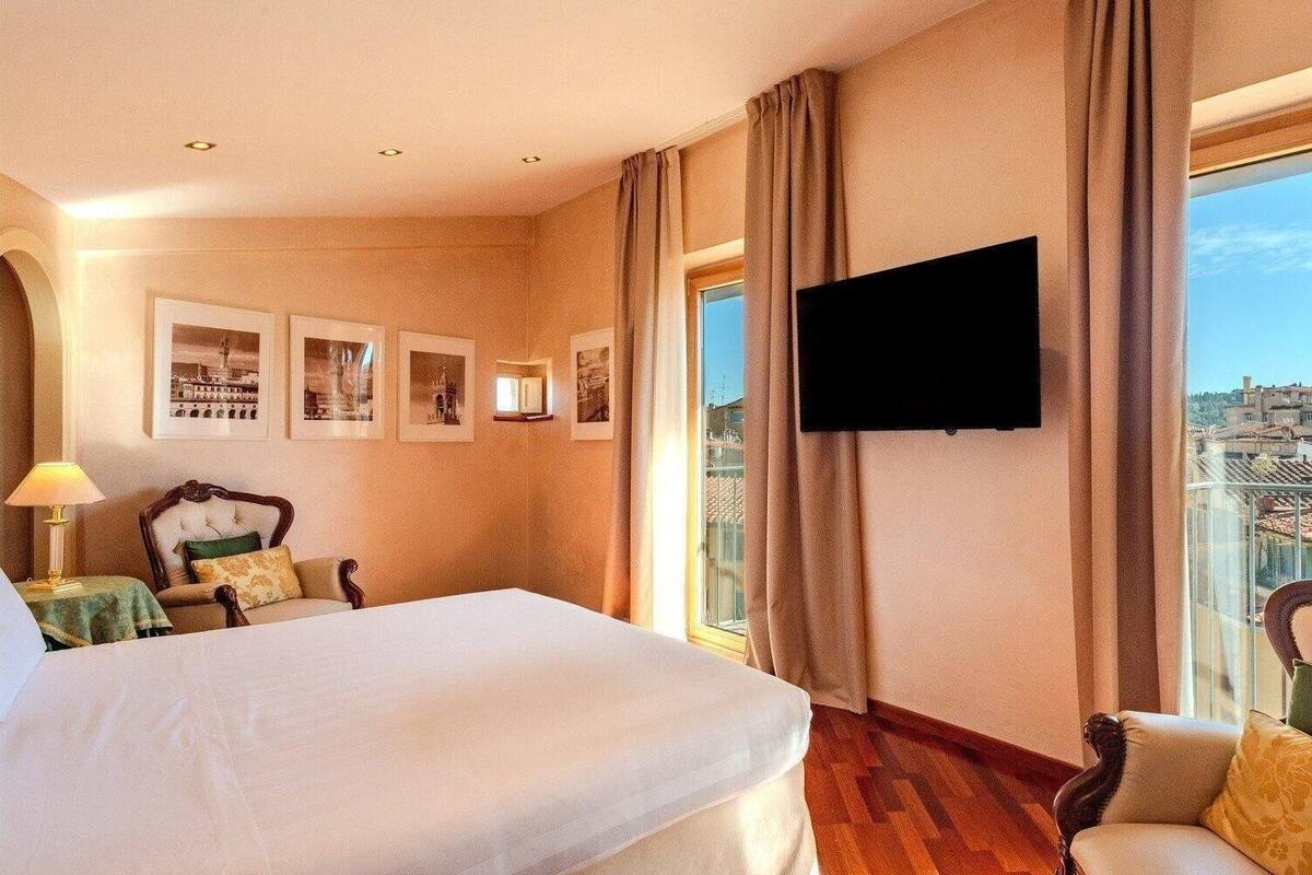 A hotel room with a large bed, a chair, a TV mounted on the wall, and framed pictures on the wall.
