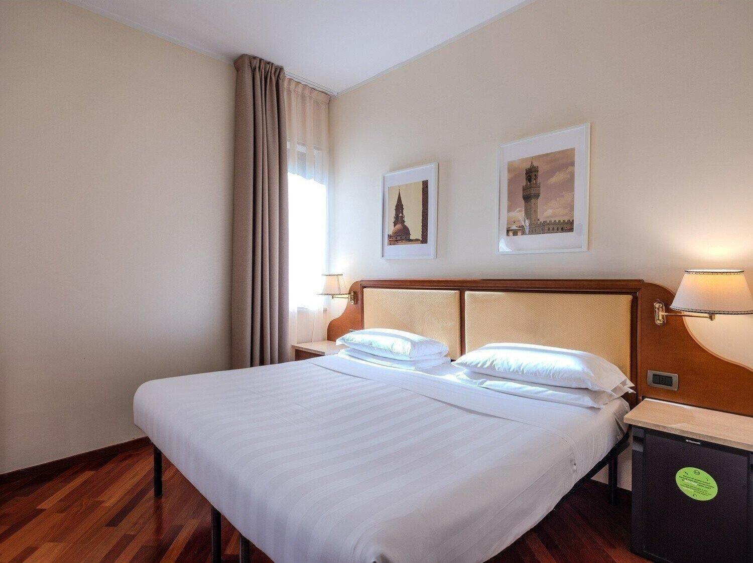 Una habitación de hotel con una cama grande, dos mesitas de noche y una lámpara fijada a la pared.