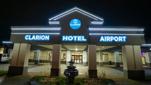Fachada del hotel Clarion Airport iluminada de noche, con señalización brillante.