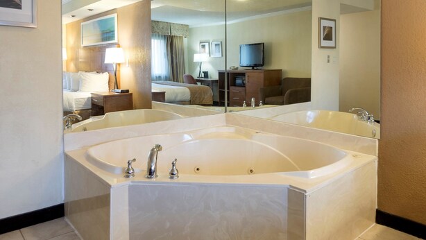 Un baño de hotel con una bañera grande, un espejo, una cama, un escritorio y un televisor.