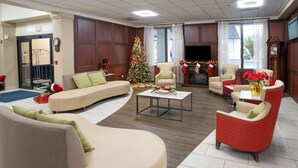 Un vestíbulo de hotel con un sofá curvo, sillones, una mesa de centro, un árbol de Navidad y una chimenea.