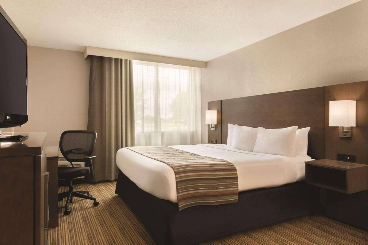 Habitación de hotel con una cama grande, un escritorio con una silla, un televisor y dos lámparas de noche.