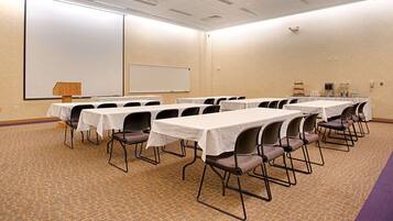 A conference room with multiple tables and chairs, a whiteboard, and a projector screen.