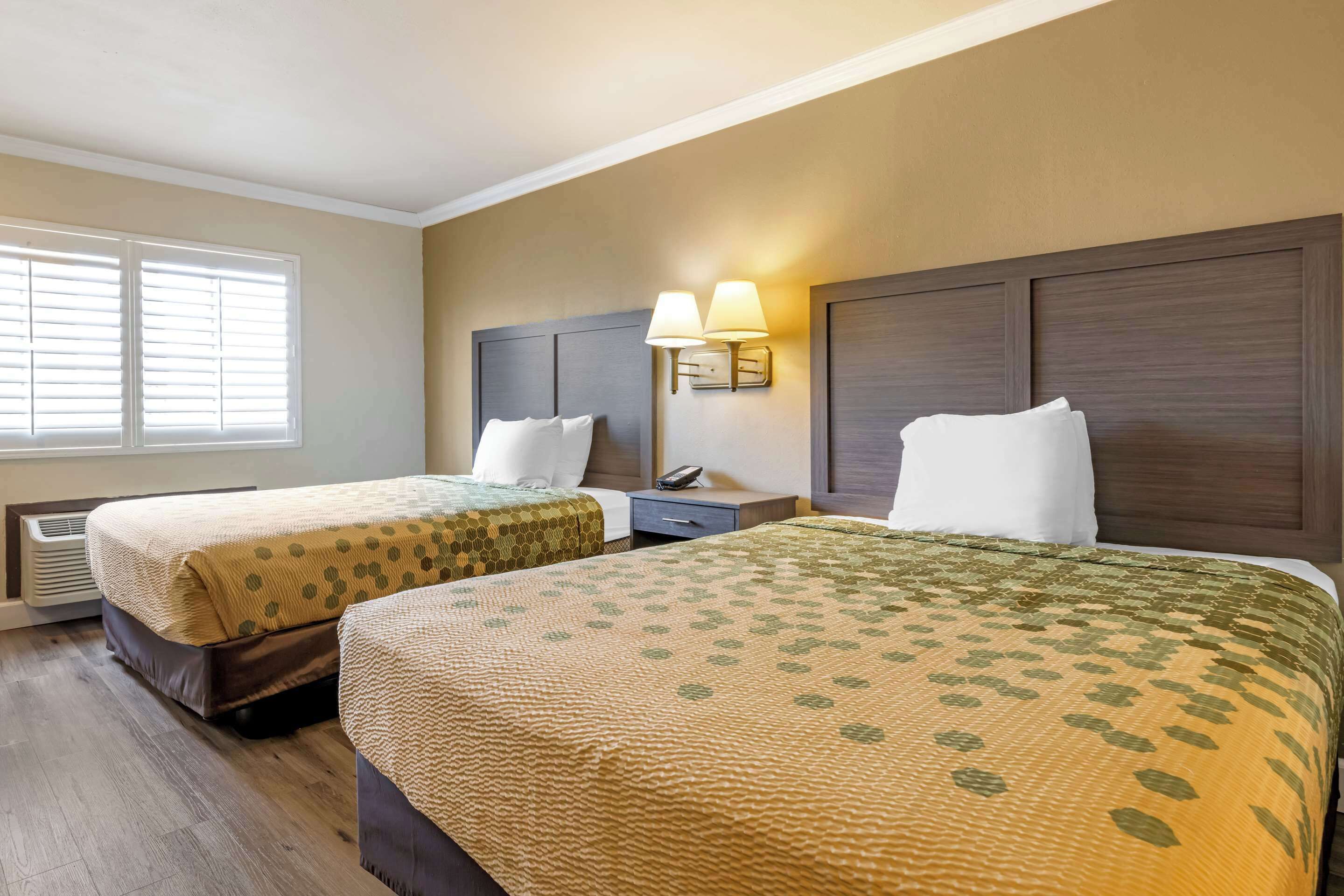 Een hotelkamer met twee bedden, een nachtkastje, een lamp en een raam met jaloezieën.