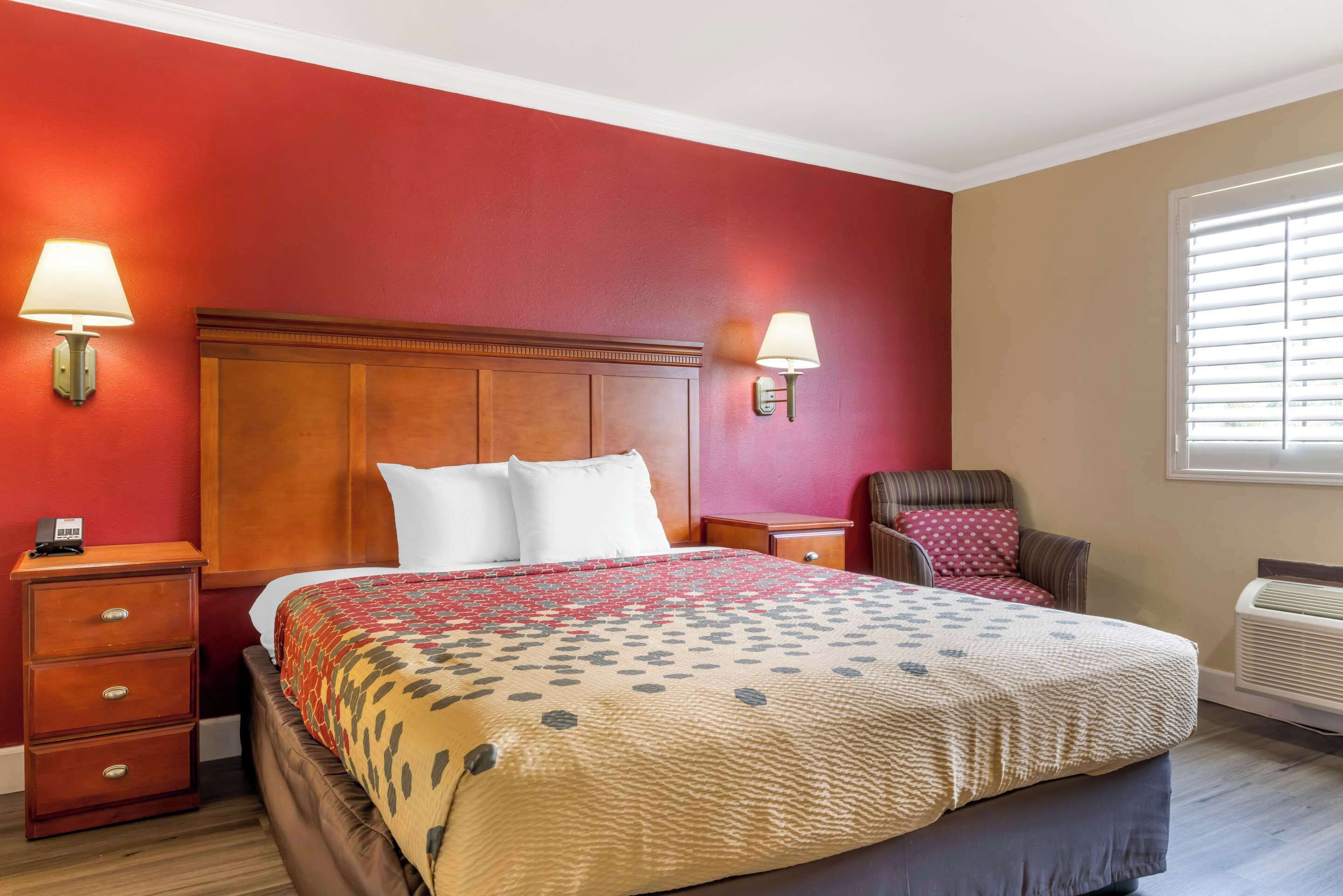 Quarto de hotel com uma cama grande, duas mesas de cabeceira, uma cadeira, uma janela com persianas e um aquecedor fixado na parede.