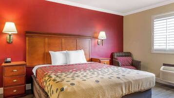 Quarto de hotel com uma cama grande, duas mesas de cabeceira, uma cadeira, uma janela com persianas e um aquecedor fixado na parede.
