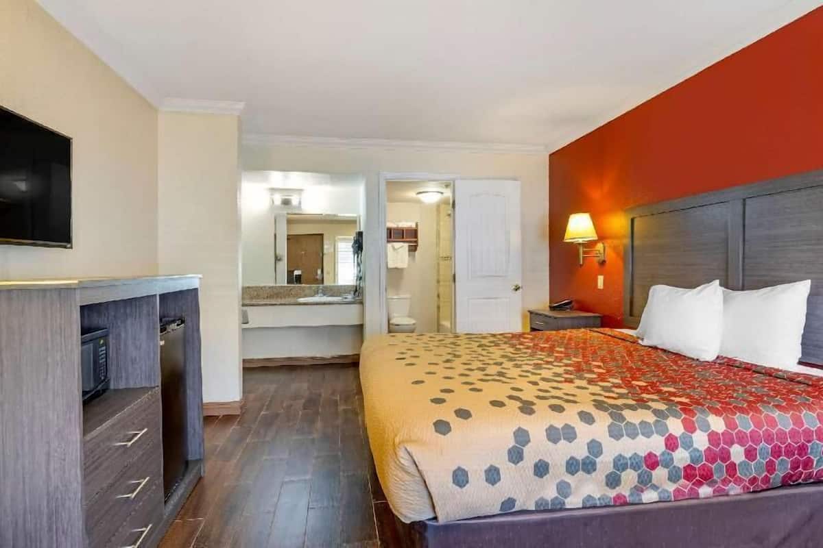 A hotel room with a bed, a desk, a television, and a bathroom visible through an open door.
