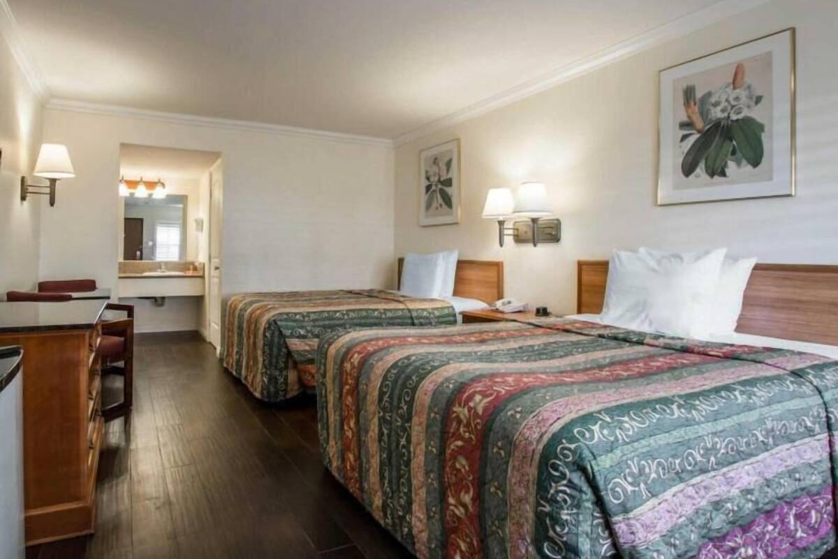 A hotel room with two beds, a desk, a chair, a mirror, and a bathroom.