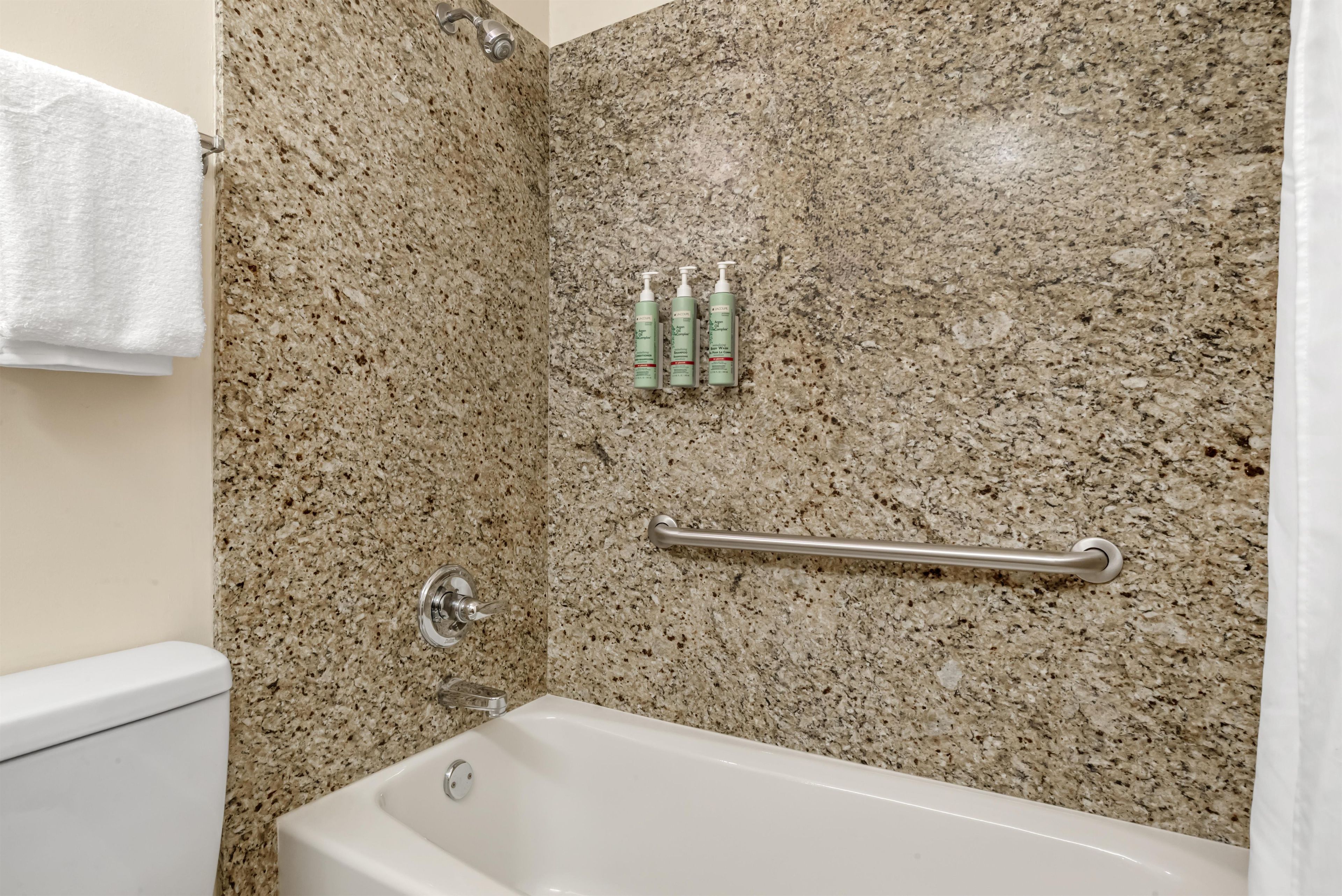 A bathroom with a white bathtub, granite walls, a towel rack, and toiletries.