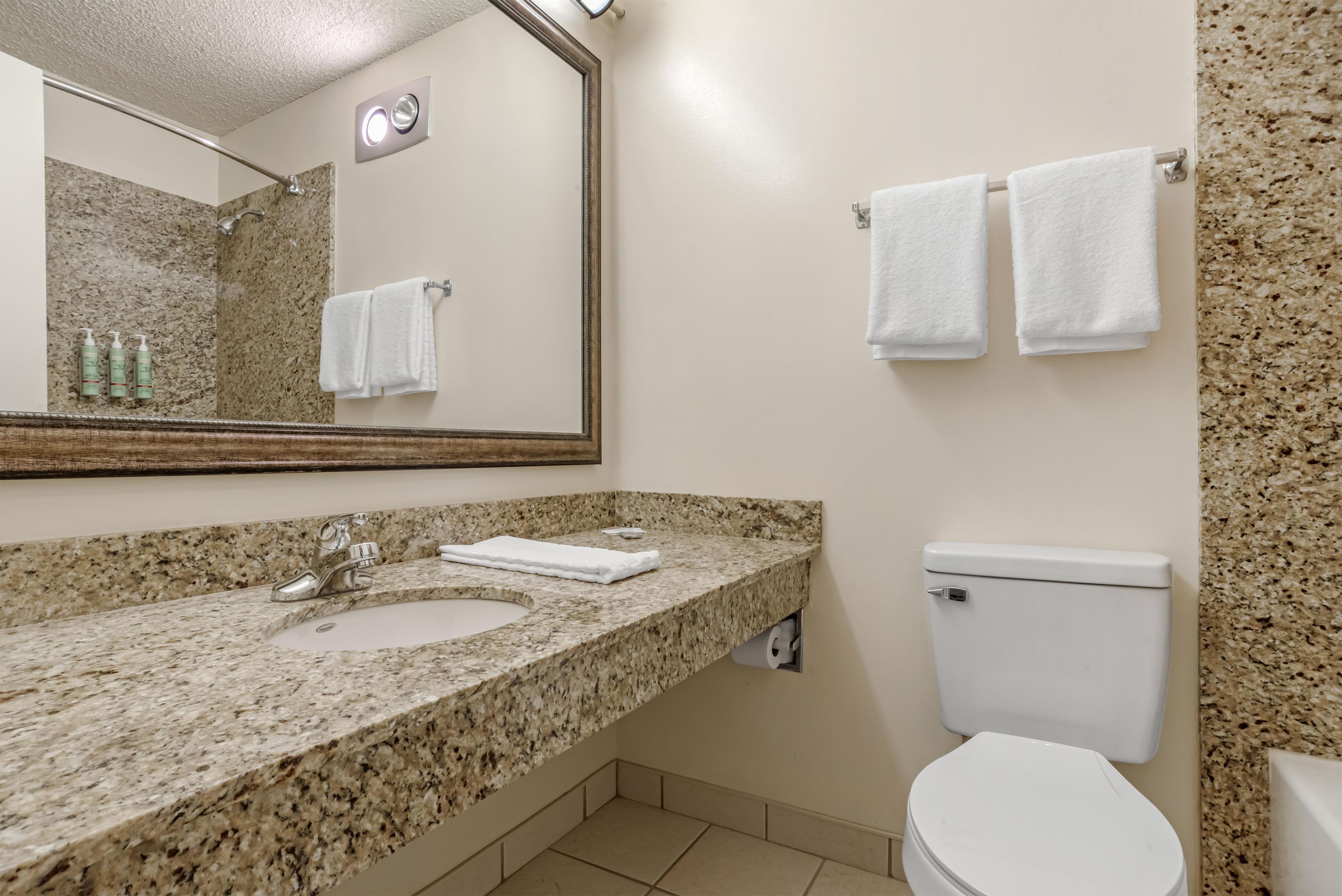 A bathroom with a granite countertop, a sink, a mirror, a toilet, and two towels hanging on the wall.