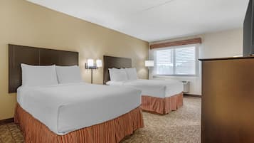 A hotel room with two beds, a wooden headboard, a window with blinds, and a flat-screen TV.