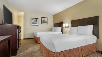 A hotel room with two beds, a desk, a television, and two framed pictures on the wall.